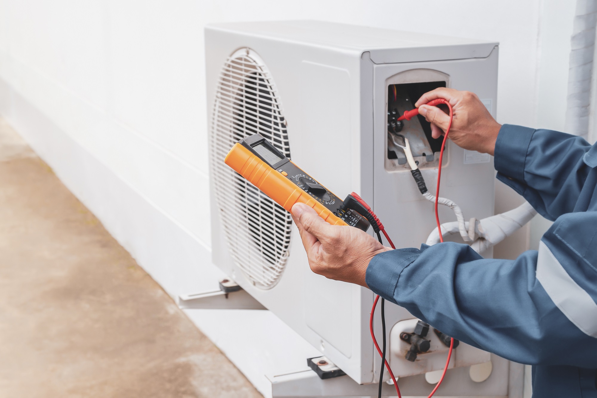 Hands of a worker testing AC condenser unit with a multimeter.