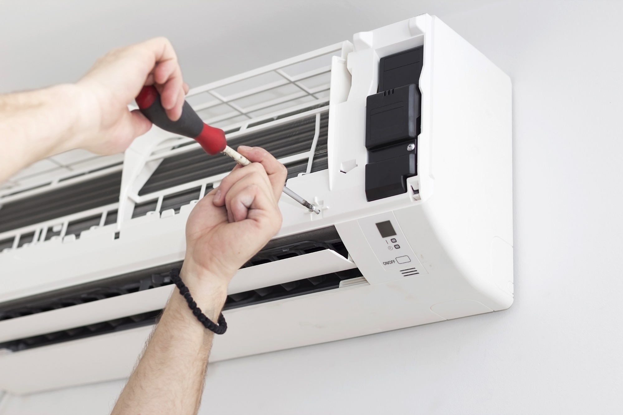 Hands using a screwdriver to fix a white mini-split AC unit.